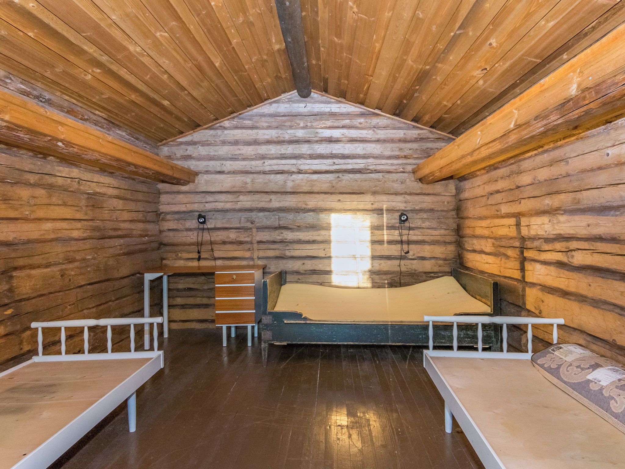 A log cabin room with a bed, two benches, and a window.