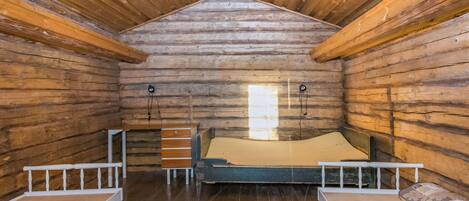 A log cabin room with a bed, two benches, and a window.