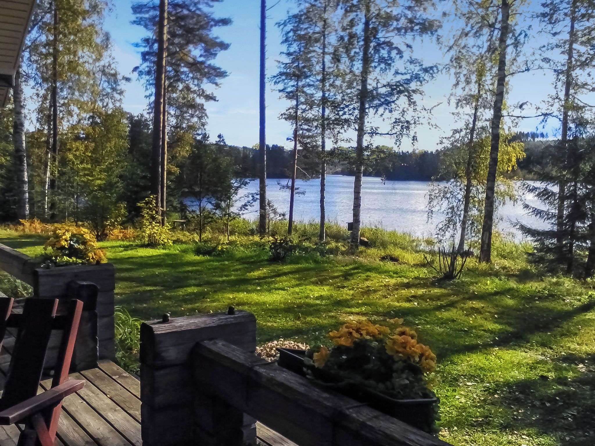 Une terrasse dotée de meubles en bois, donnant sur un lac entouré d’arbres.