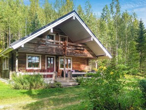 A two-story log cabin with a steeply pitched roof, a front porch with seating, and a surrounding forest. - Saarijärvi by Interhome (Sulkava)