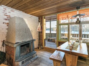 A rustic cabin interior with a stone fireplace, wooden flooring, a wooden table with a bench, and a view of a snowy landscape through large windows. - Saarijärvi by Interhome (Sulkava)
