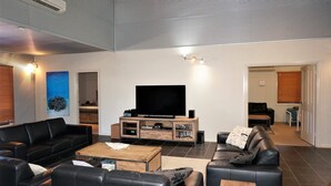 A modern living room with a flat-screen TV, leather sofas, a wooden coffee table, and a bookshelf. - 2 Trout Place - large well appointed home (EXMOUTH)