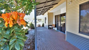 A covered outdoor area with a wooden deck, a bench, and a view of a residential building. - 2 Trout Place - large well appointed home (EXMOUTH)