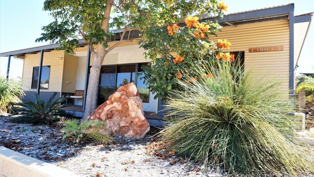 A modern building with a large rock feature, a tree with orange flowers, and a spiky plant in the foreground. - 2 Trout Place - large well appointed home (EXMOUTH)