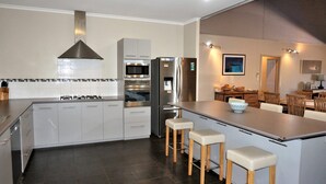 A modern kitchen with grey cabinets, stainless steel appliances, and a central island with bar stools. - 2 Trout Place - large well appointed home (EXMOUTH)