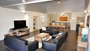 A spacious living room with a flat-screen TV, leather sofas, and a dining area with wooden furniture. - 2 Trout Place - large well appointed home (EXMOUTH)