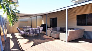 An outdoor patio with a wooden deck, a dining table with striped chairs, and a wicker sofa.