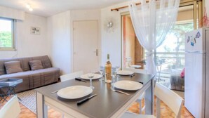 A dining area with a table set for two, a sofa, and a refrigerator.