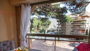 A room with a balcony overlooking a street and buildings, a table with a fruit bowl, and a red sofa.