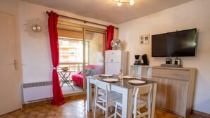 A compact kitchen with a dining table, chairs, a refrigerator, and a TV mounted on the wall.