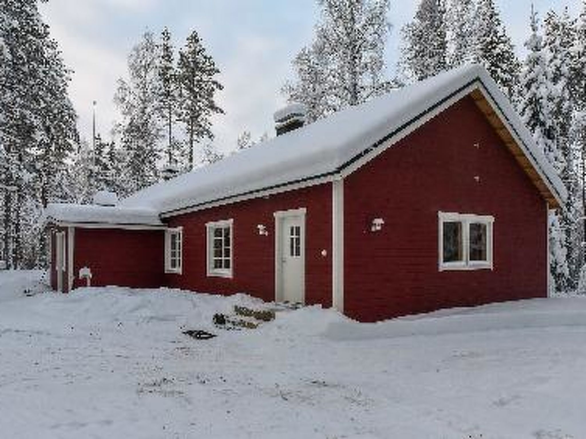 Eine rote Holzhütte mit verschneitem Dach, umgeben von schneebedeckten Bäumen.