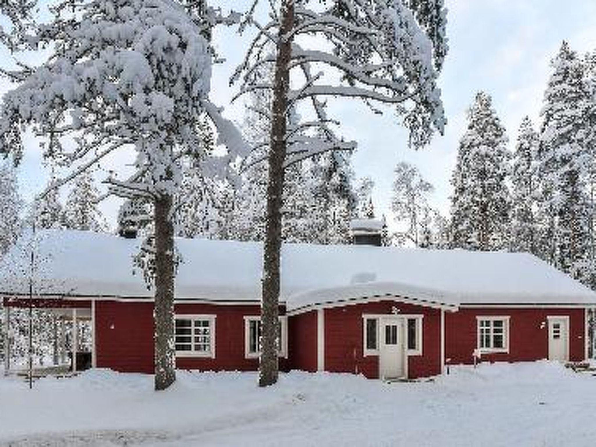 A red wooden cabin surrounded by snow-covered trees.