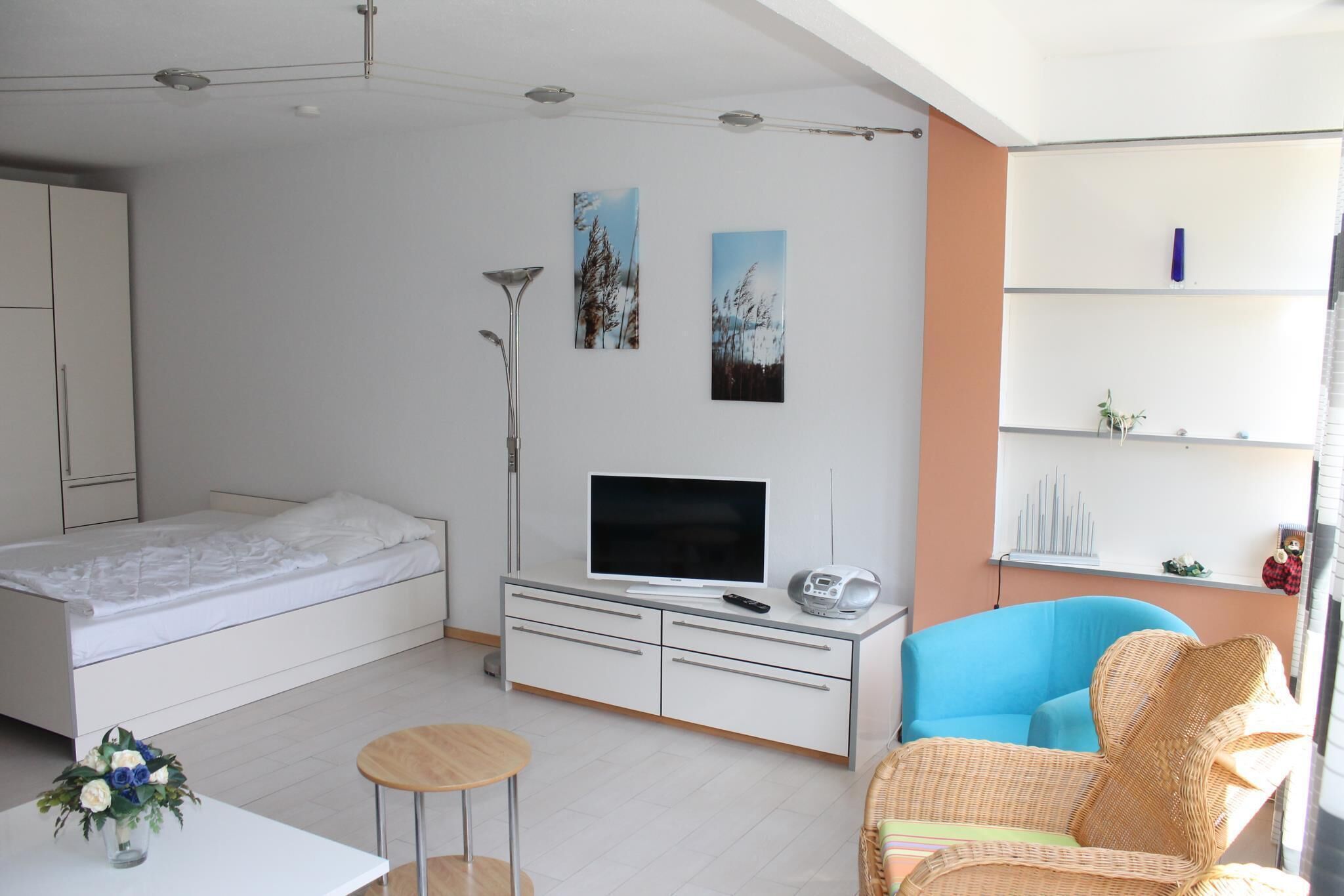 A modern bedroom with a bed, a TV, a dresser, and a blue chair.