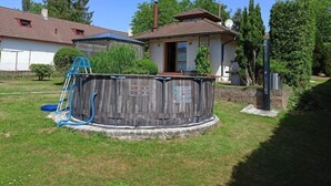 Un patio trasero con un hidromasaje de madera, una manguera azul y un cobertizo pequeño.