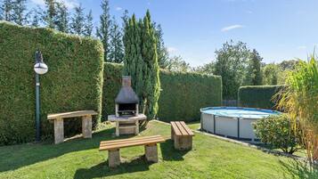 A backyard with a barbecue grill, picnic tables, a swimming pool, and a well-maintained hedge.