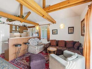 A cozy living room with a wooden ceiling, a sofa set, a small table, and a bar area with stools.