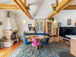A cozy living room with a fireplace, a round dining table with chairs, a television, and a bookshelf.