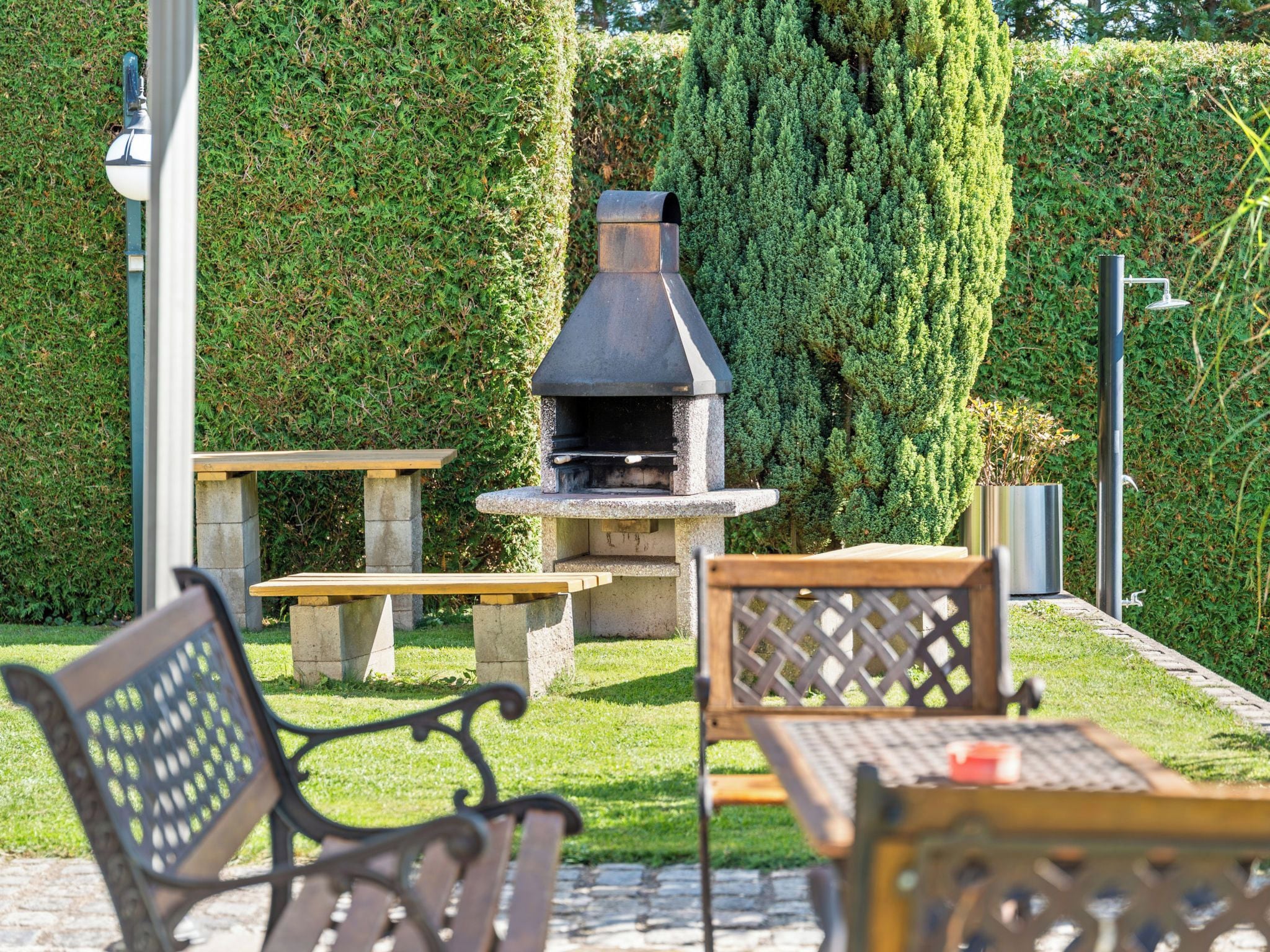 Un espace extérieur aménagé en terrasse, avec un barbecue en pierre, deux tables en bois et des chaises en métal.