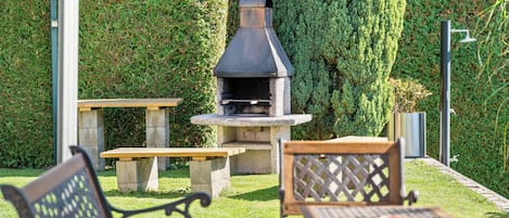 An outdoor patio area with a stone barbecue grill, two wooden tables, and metal chairs.