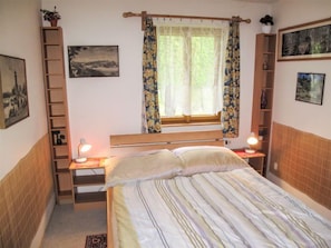Ein Schlafzimmer mit einem Bett, zwei Nachttischen, einem Fenster mit Vorhängen, einer Holzleiter und Wandregalen.