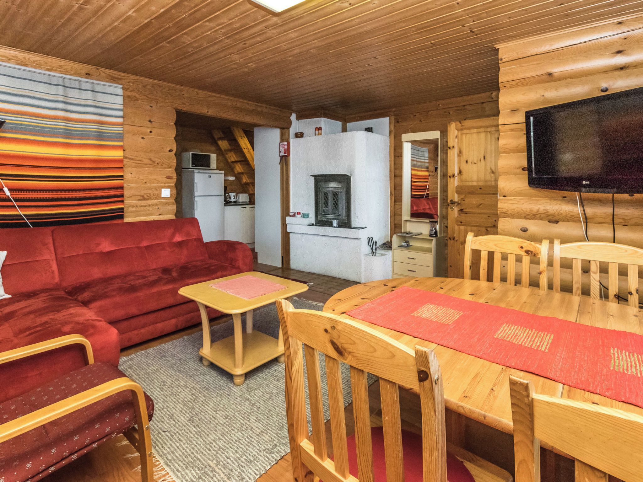 A cozy cabin interior with a wooden dining table, red sofa, and a television.