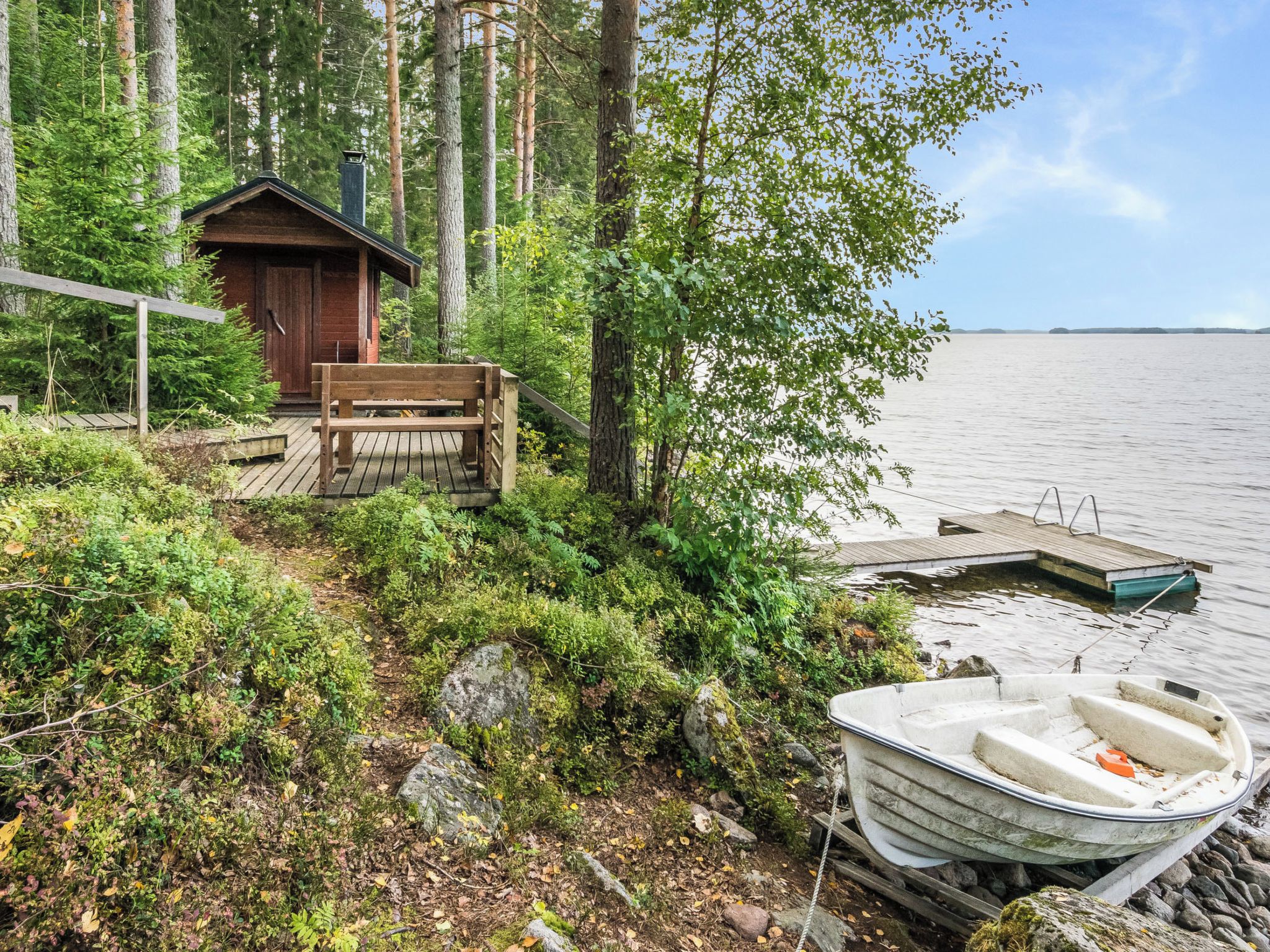 Une cabane avec un quai, entourée d’une forêt dense et bordant un lac paisible.