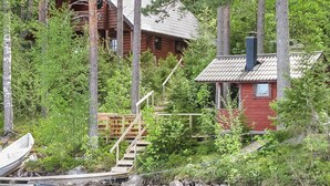 A cabin surrounded by dense forest, with a dock extending into a calm body of water.