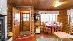 A cozy cabin interior with a wooden interior, a fireplace, a dining area with chairs and a table, and a television mounted on the wall.