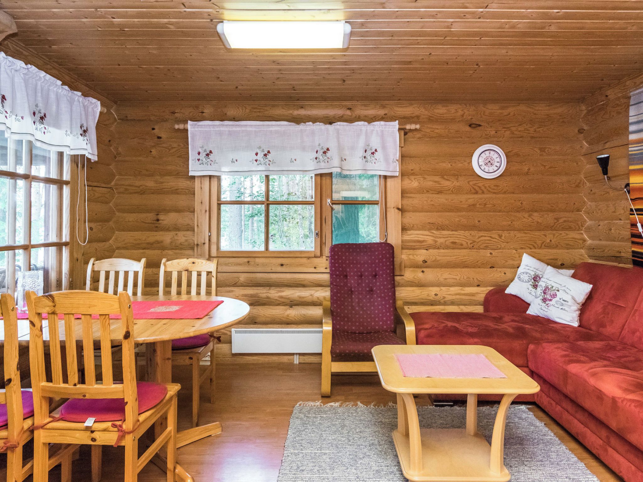 Ein gemütliches Blockhaus-Interieur mit einem Esstisch, Stühlen, einem roten Sofa und einem kleinen Teppich.