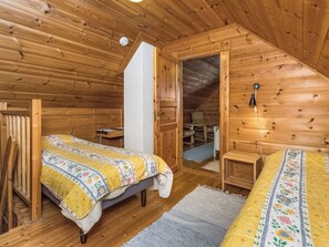A cozy wooden cabin bedroom with two beds, a small table, and a chair.