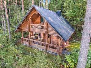 En træhytte med balkon, omgivet af skov.