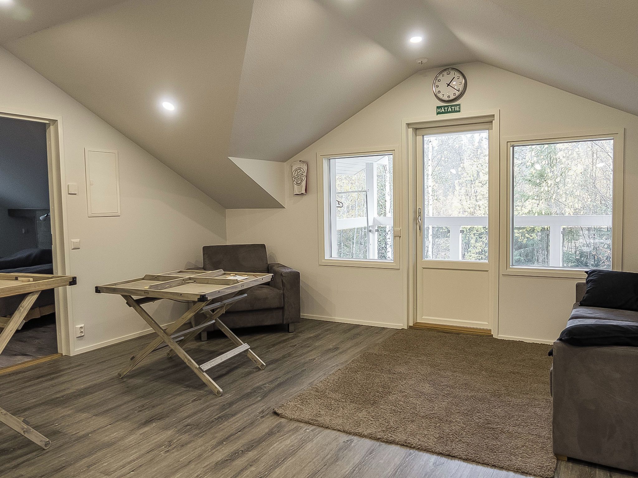 Une chambre à coucher aménagée dans un grenier, avec un plafond en pente, un établi en bois, un canapé et une grande fenêtre donnant sur la forêt.