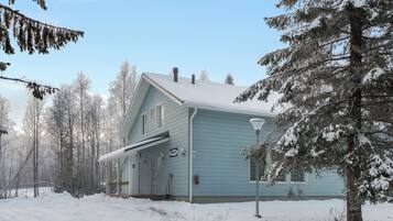 Et lyseblåt hus med en veranda, omgivet af sneklædte træer.