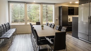 A modern kitchen with a large dining table, built-in appliances, and a view of a forest through large windows.
