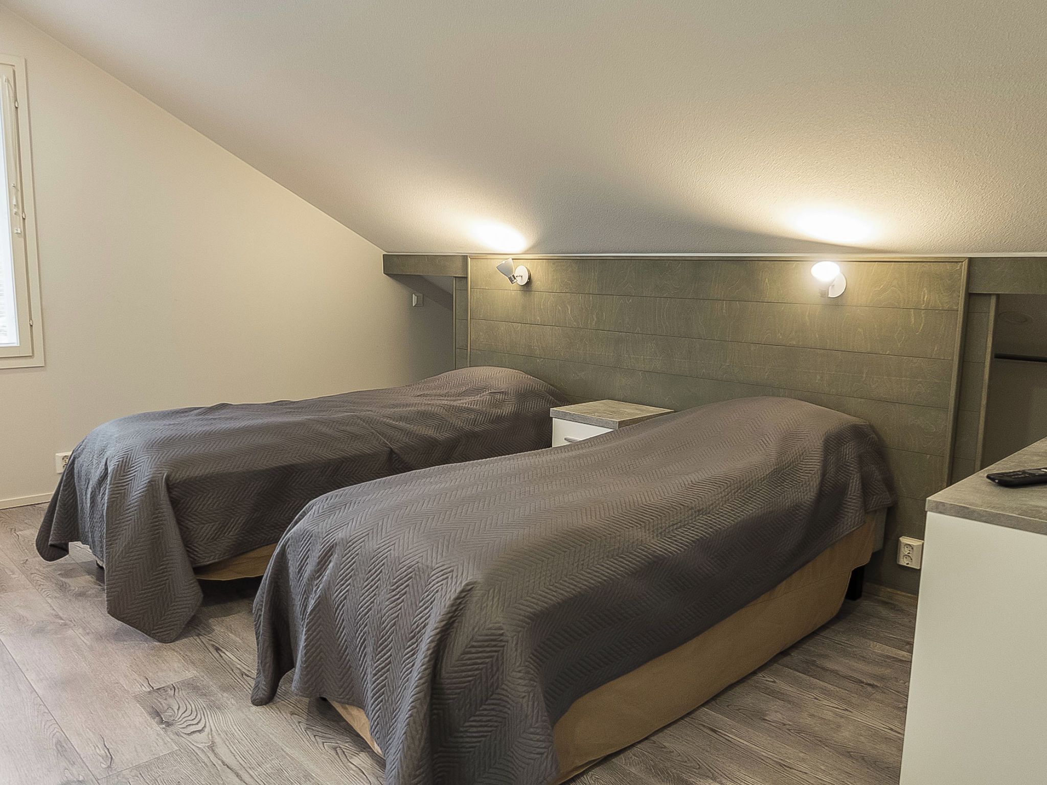 Un dormitorio con dos camas individuales, un cabecero de madera, una mesita de noche pequeña y un buró.