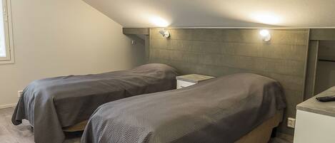 Ein Schlafzimmer mit zwei Einzelbetten, einem Holzkopfteil, einem kleinen Nachttisch und einem Beistelltisch.