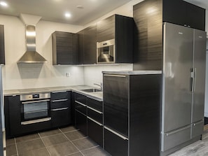 A modern kitchen with stainless steel appliances, dark cabinetry, and a tiled backsplash.