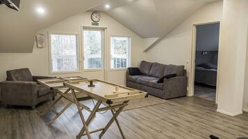 Avoin, loft-tyylinen huone, jossa on puinen pöytä, kaksi sohvaa ja näkymä parvekkeelle.