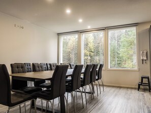 Uma sala de conferências com uma mesa comprida e cadeiras, amplas janelas com vista para árvores e piso em tons claros.