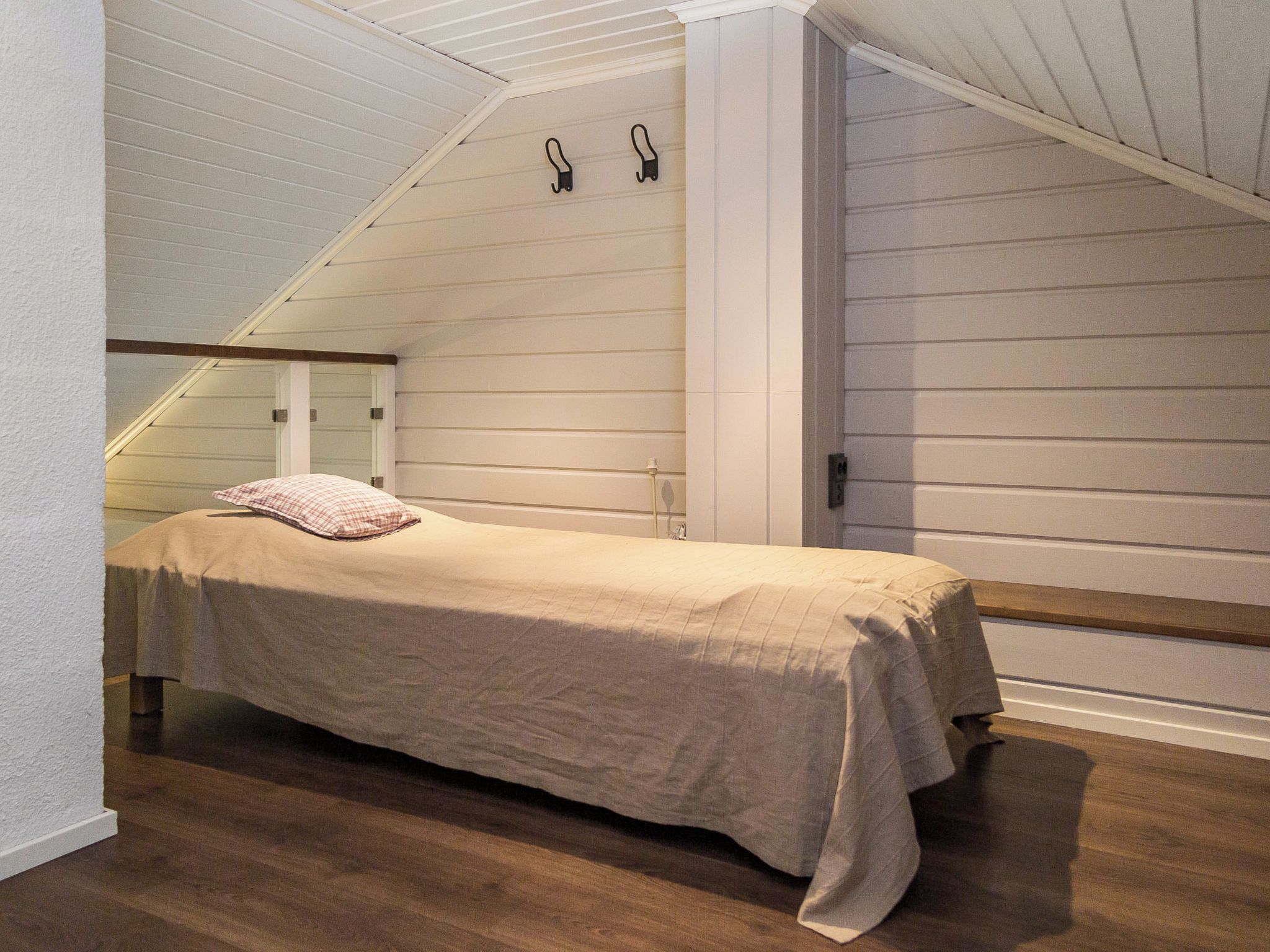 A bedroom with a bed, a wooden floor, and a sloped ceiling.