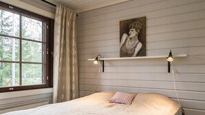 Een slaapkamer met een groot raam, een bed met een geruit kussen en twee wandlampen.