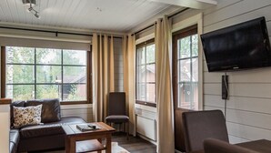 Een gezellige woonkamer met een bank, een fauteuil, een salontafel en een aan de muur bevestigde televisie.