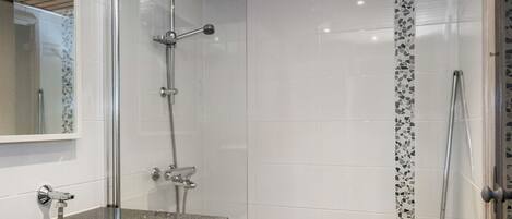 A modern bathroom with a shower, a vanity with a mirror, and a tiled floor.