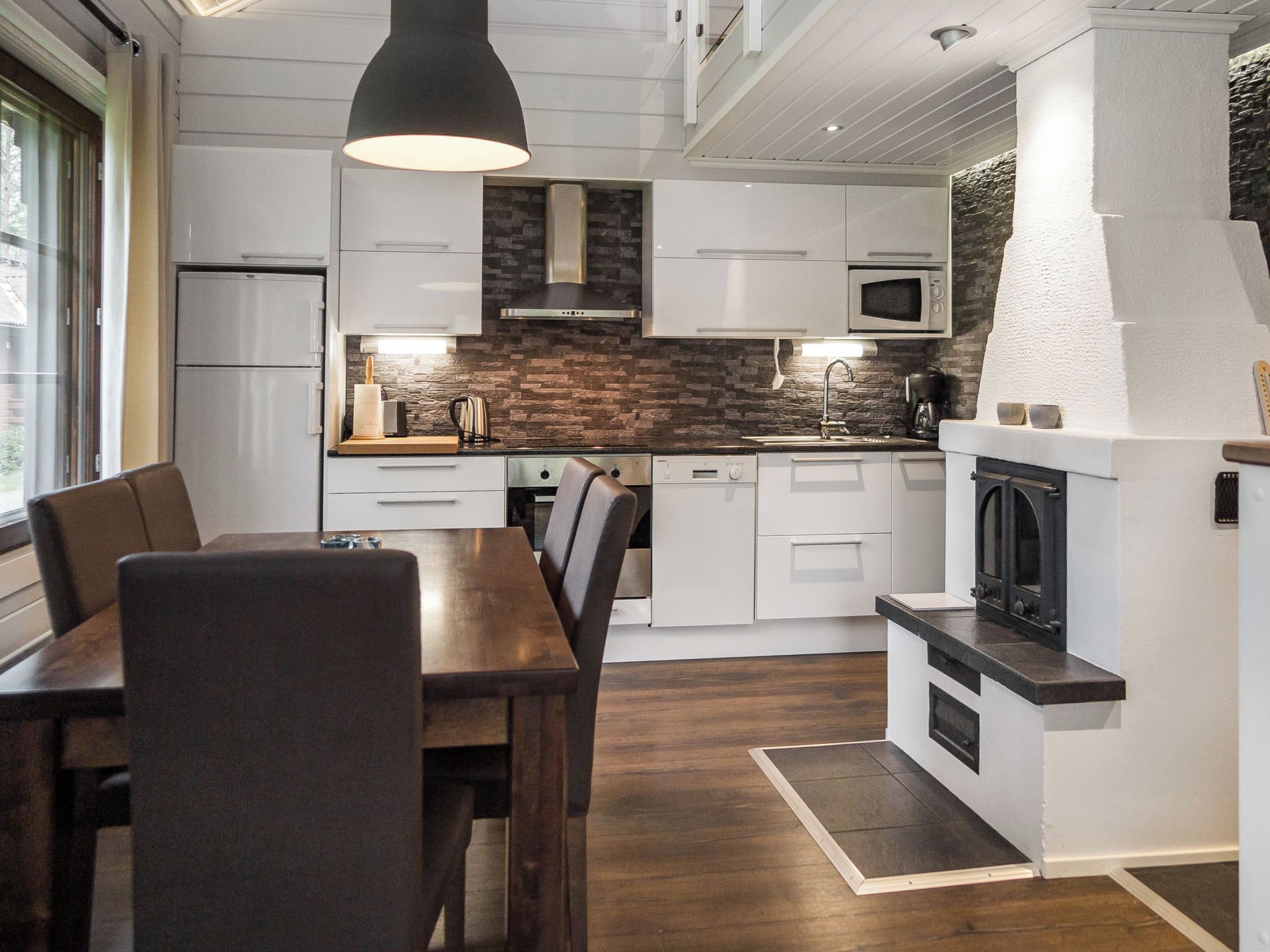 A modern kitchen with white cabinets, a stone backsplash, and a black pendant light.