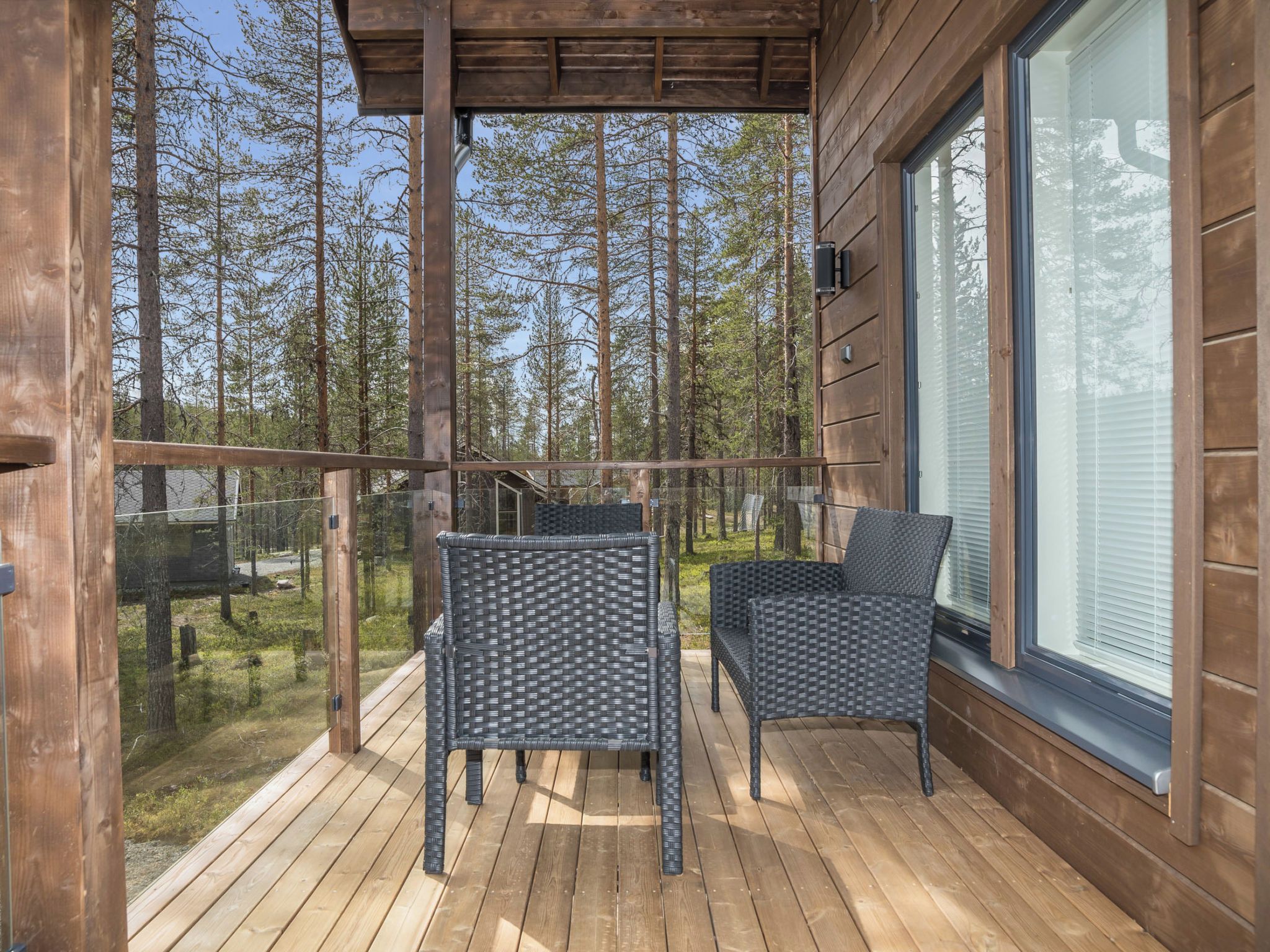 A wooden deck with two wicker chairs and a glass railing overlooking a forest.