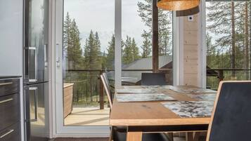 A modern kitchen with a refrigerator, a dining area with a table and chairs, and a large window with a view of trees.