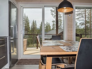 A modern kitchen with a refrigerator, a dining area with a table and chairs, and a large window with a view of trees.