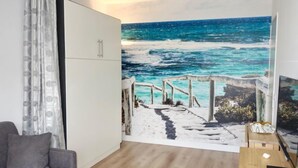 A living room with a large ocean mural, a grey sofa, a wooden coffee table, and a white cabinet. - Sun Beach by Interhome (Arcachon)