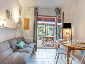 A living room with a sofa, a dining table with chairs, a TV, and a view of the outdoors.