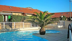 Ein Swimmingpool mit einer Palme, umgeben von einem weißen Zaun und Gebäuden mit roten Ziegeldächern.